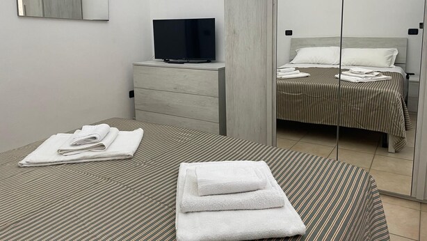 A hotel room with a bed, a TV on a dresser, and a mirror reflecting the room.