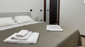 A neatly made bed with white linens, a striped bedspread, and a stack of folded towels on the floor.