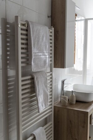 A modern bathroom with a wooden vanity, a white sink, and a towel rack with two towels.