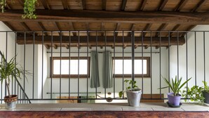Un balcon avec des poutres en bois, des plantes en pot et une vue sur une pièce dotée d’une fenêtre et d’un rideau.
