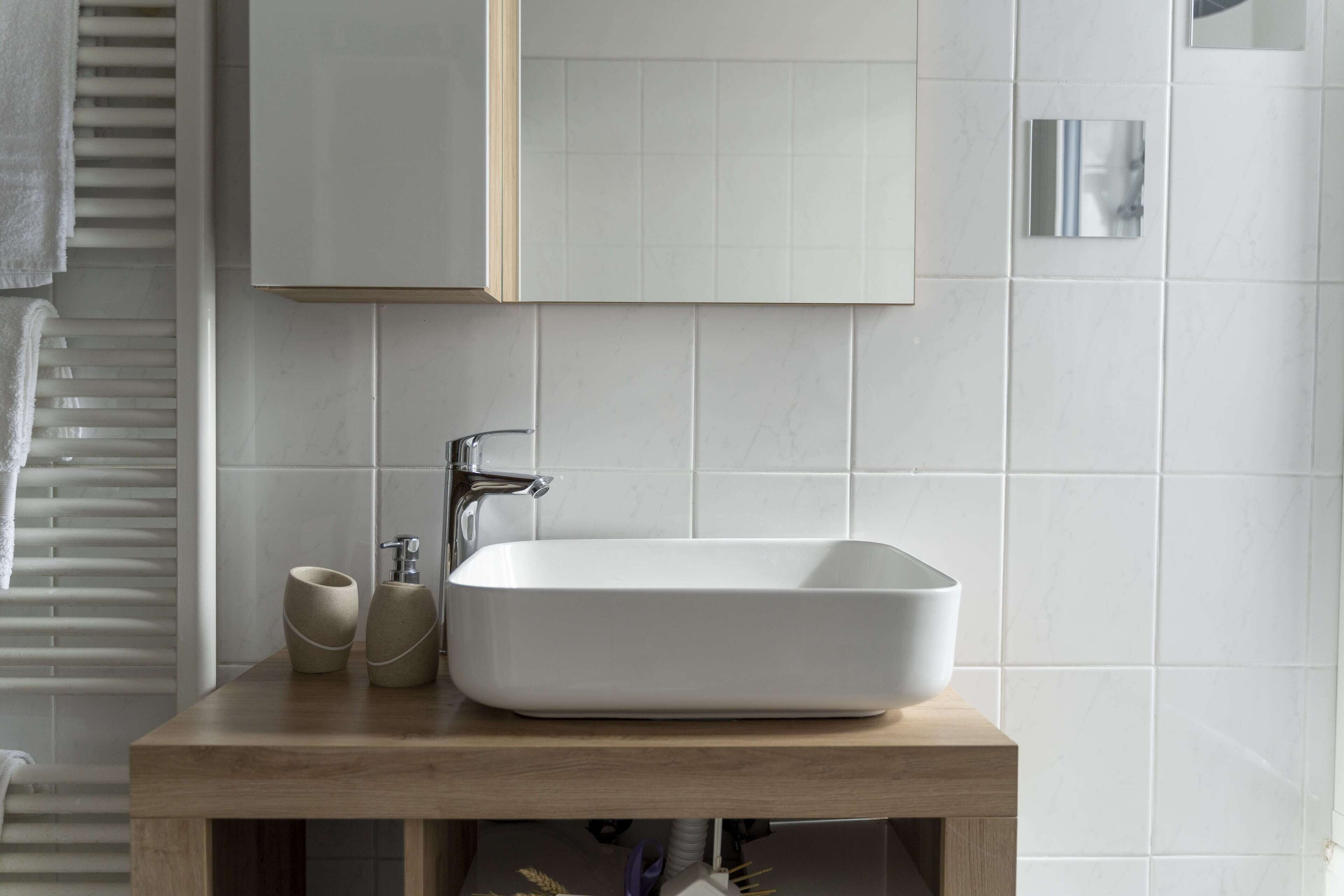 Une salle de bain avec un lavabo rectangulaire blanc, un meuble-lavabo en bois et un miroir au-dessus du lavabo.