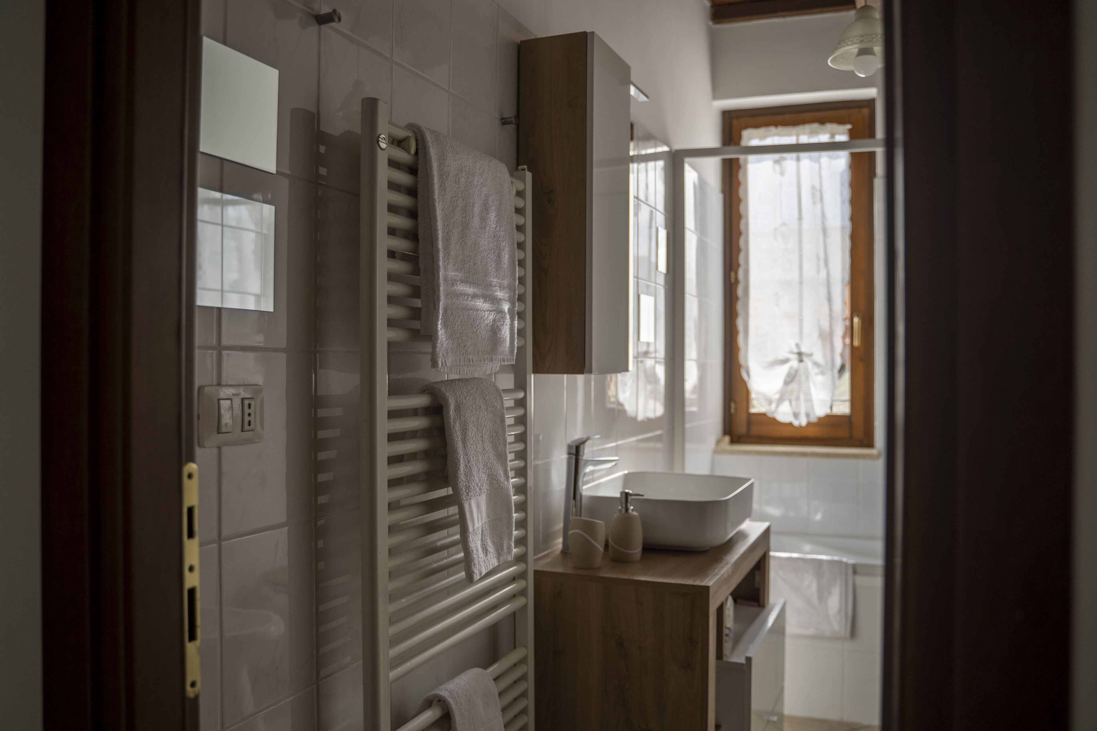 Un bagno moderno con lavandino incassato, porta asciugamani e finestra con tende.