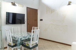 A dining area with a table and chairs, a television mounted on the wall, and a door.