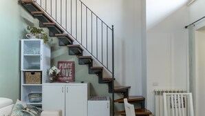 Un escalier au design moderne, un meuble blanc contenant de la verrerie, une pancarte sur laquelle on peut lire « PAIX, AMOUR, CHOCOLAT », et une nappe à motifs sur une table.