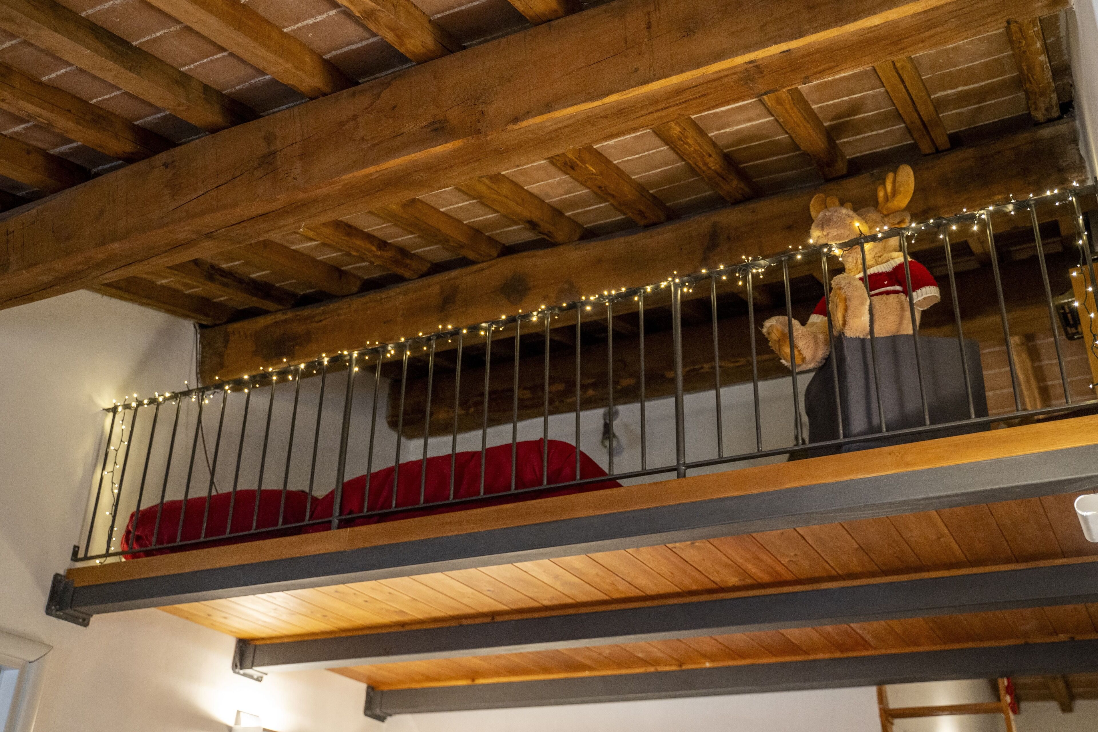 A loft-style room with a wooden ceiling, a red sofa, and a decorative stuffed animal on the railing.