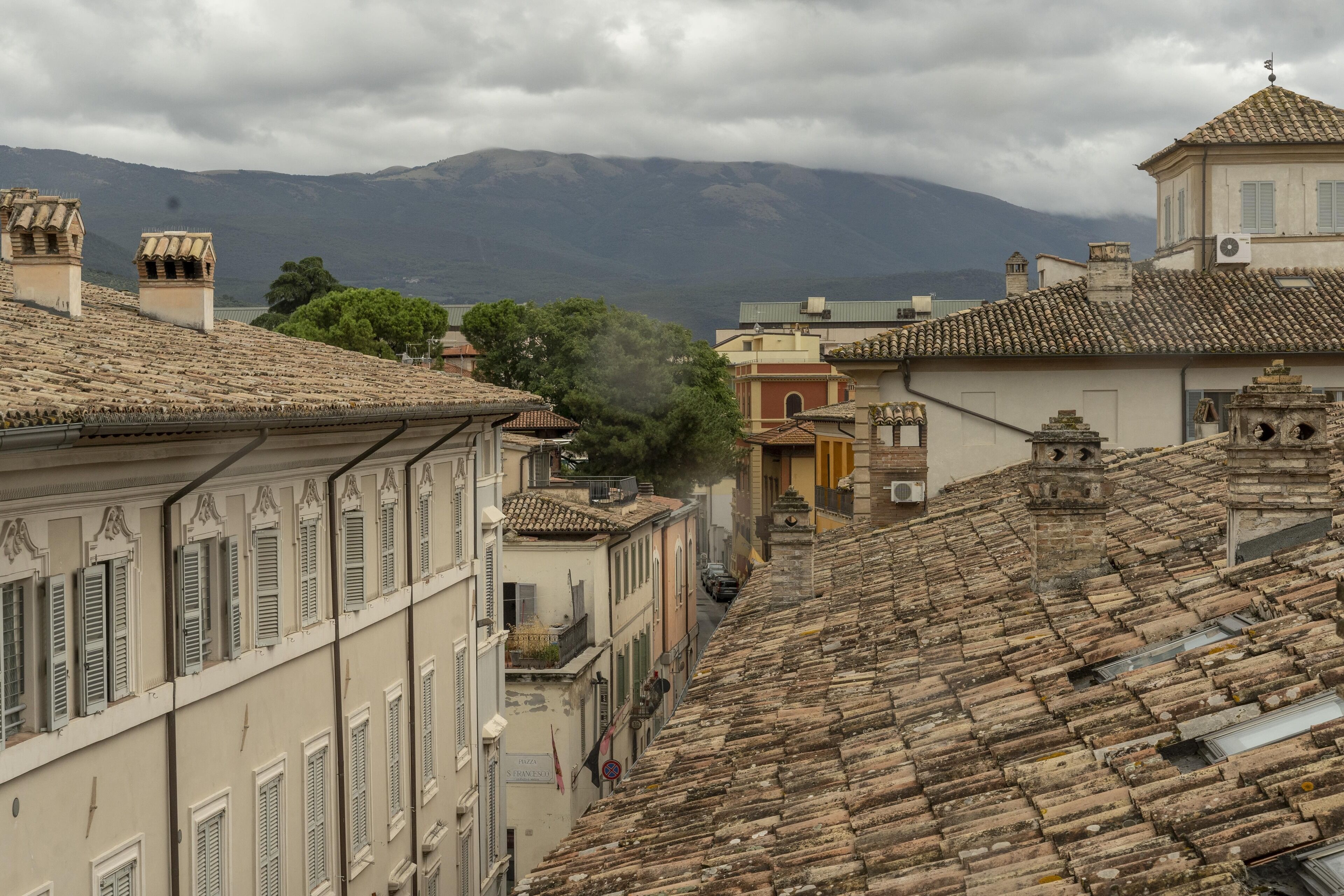 A historic town with terracotta-tiled roofs, traditional architecture, and a mountain in the background.