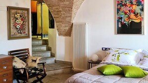 A bedroom with a bed, a chair, a dresser, a radiator, and a staircase leading to an upper level.