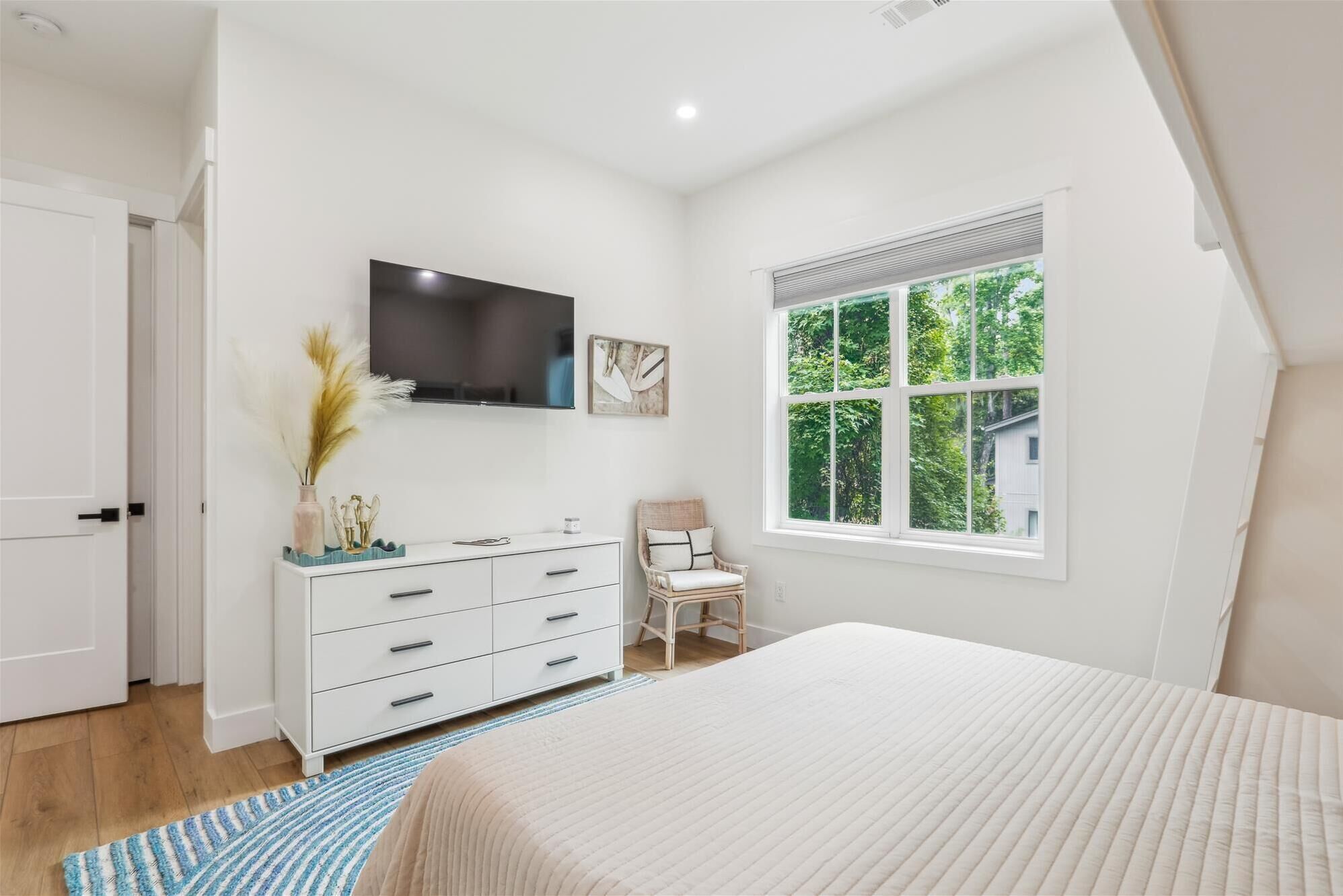 Une chambre à coucher avec un grand lit, une commode, une chaise, un téléviseur et une fenêtre donnant sur un paysage verdoyant.