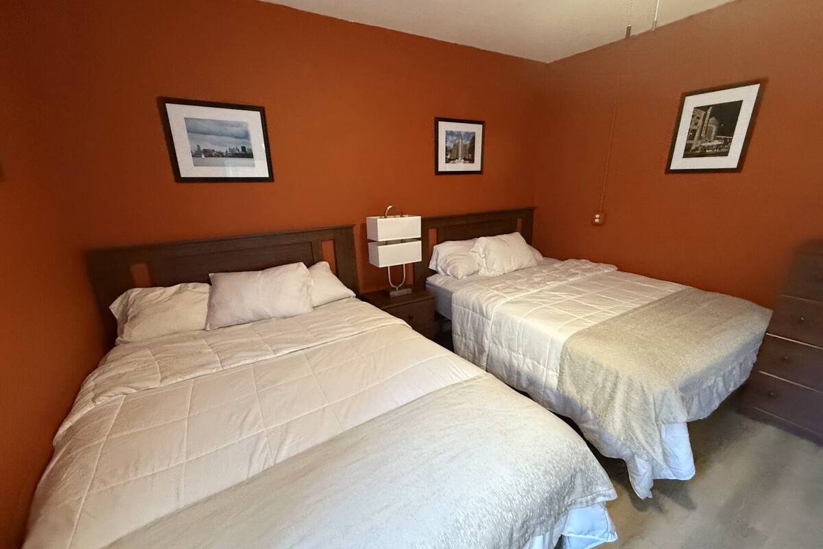 A hotel room with two beds, a nightstand with a lamp, and framed pictures on the walls.