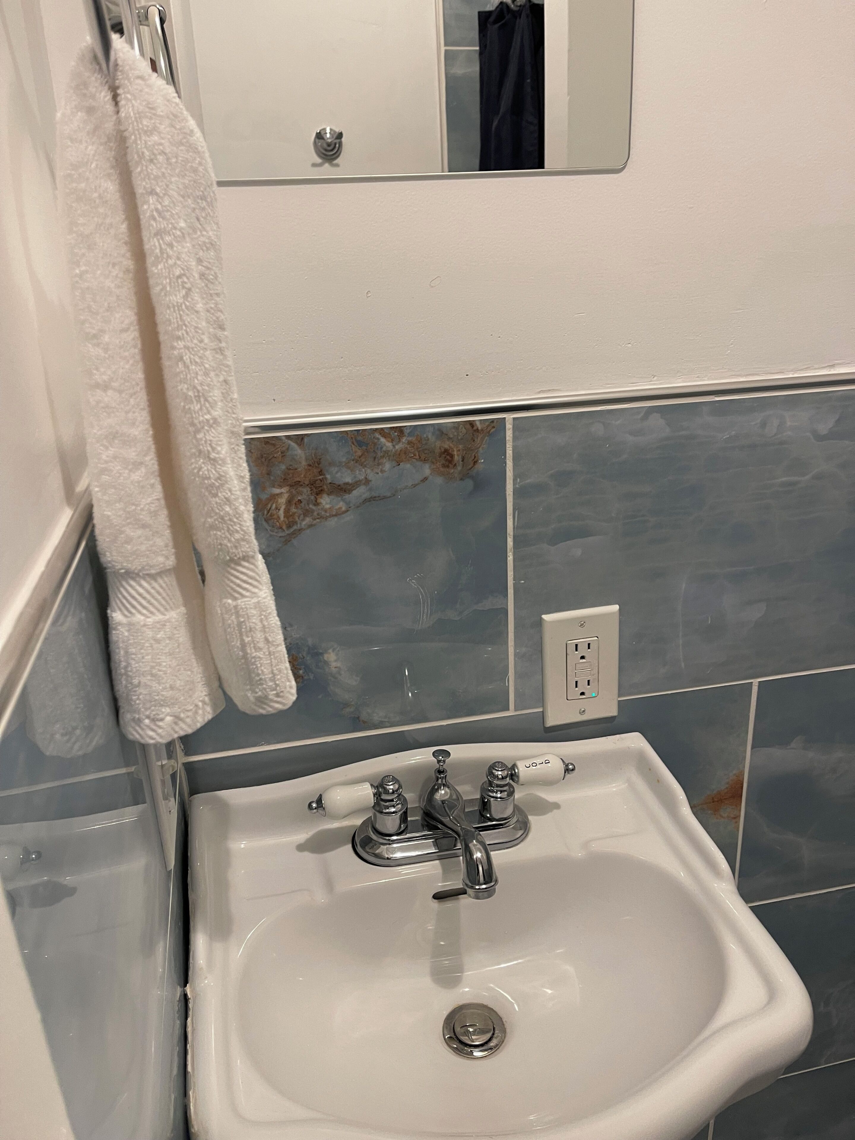 A bathroom with a white sink, a towel rack, a mirror, and blue-tiled walls.