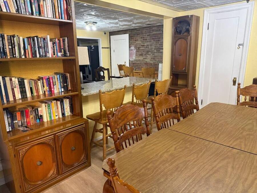 A dining area with a long wooden table and chairs, surrounded by bookshelves filled with books.