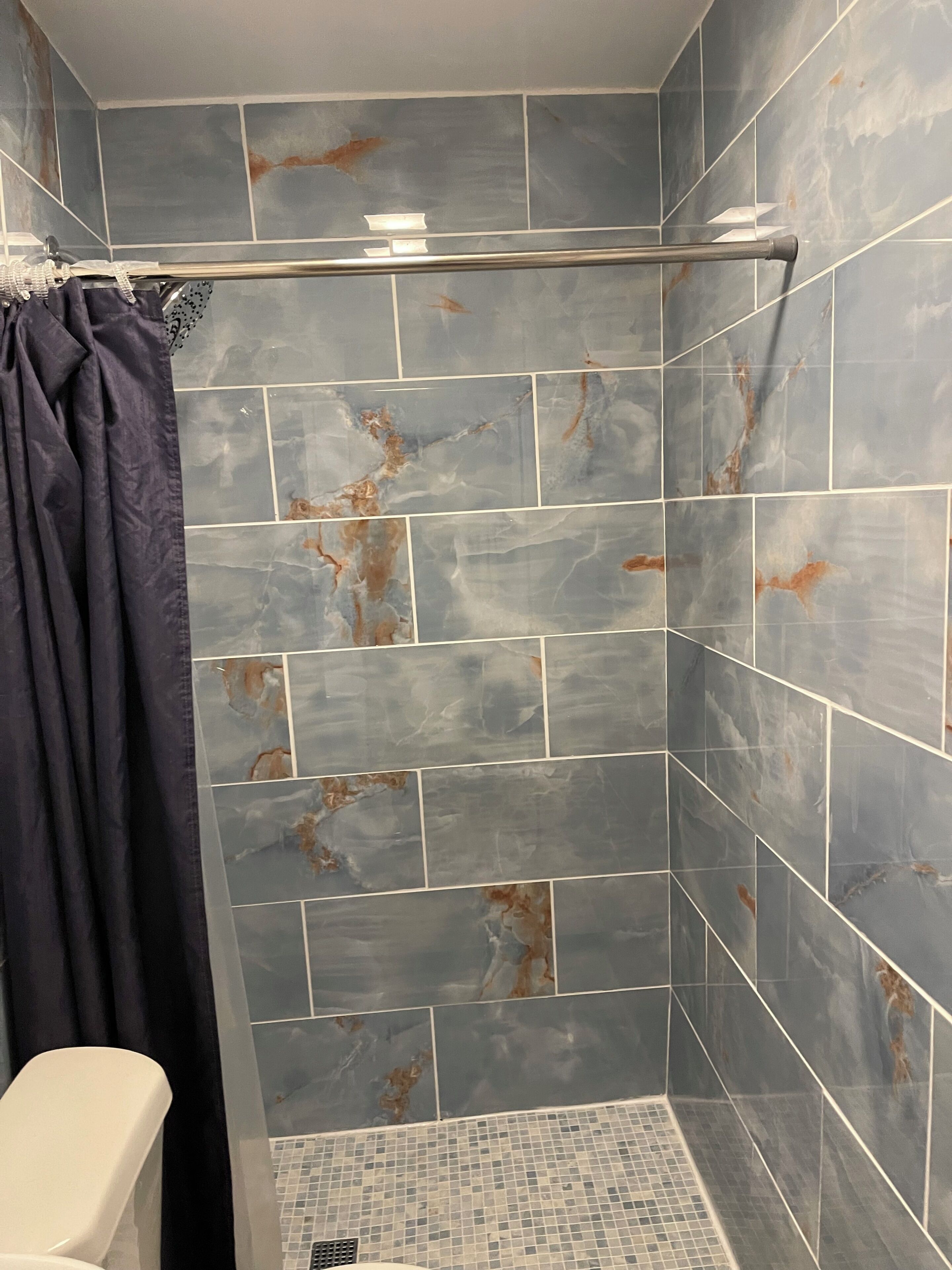 Un área de ducha con pared de azulejos, cortina de baño y un inodoro.