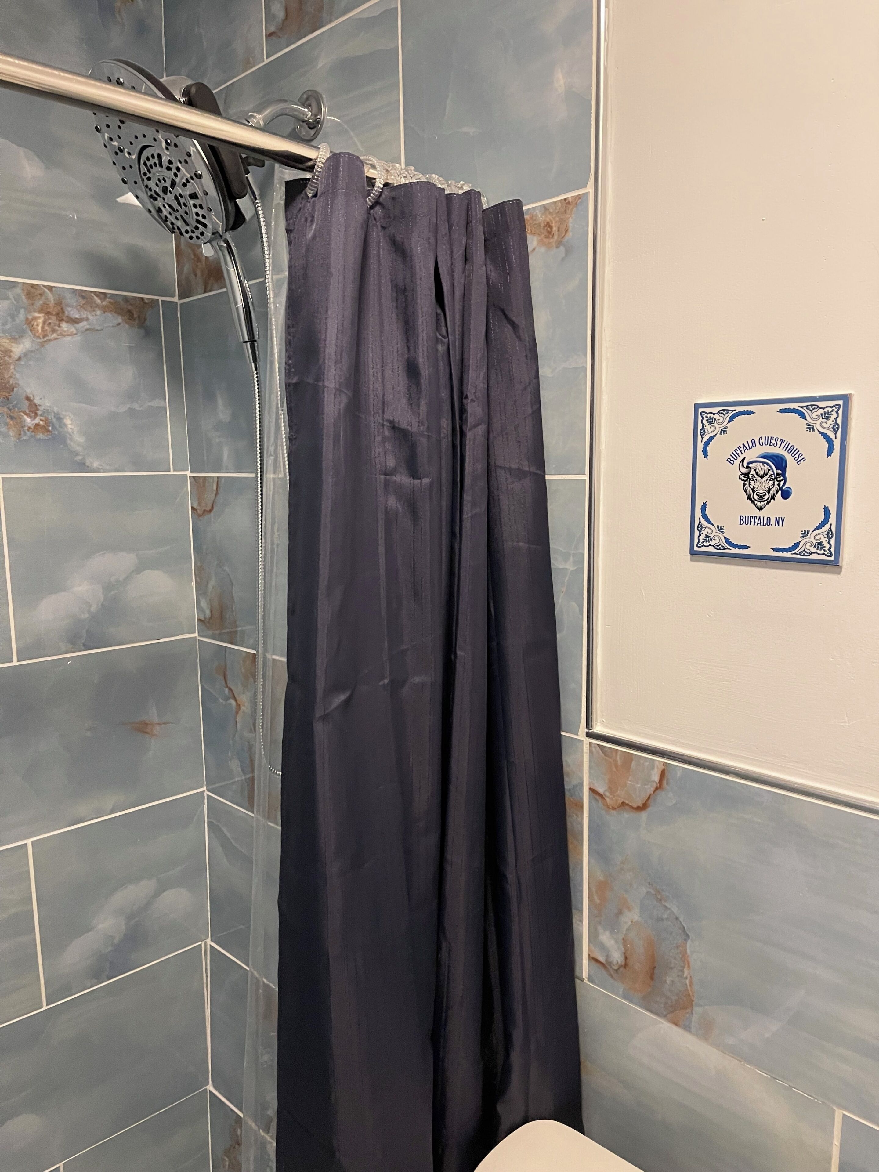 Baño con cortina de ducha, cabezal de ducha montado en la pared y un letrero que indica la ubicación como Buffalo, NY.