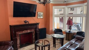 A living room with a fireplace, leather sofa, and a television mounted on the wall. - Buffalo Guesthouse (Buffalo)