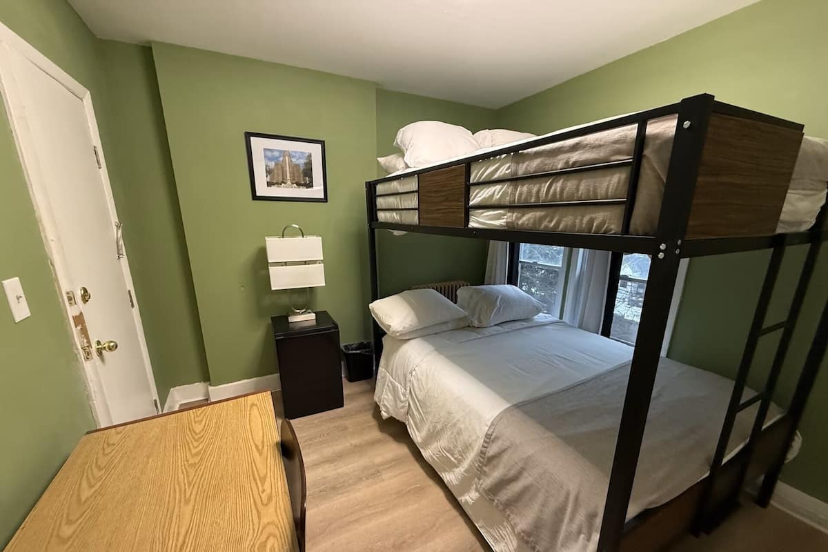 A bunk bed room with a wooden table, a nightstand with a lamp, and a framed picture on the wall.