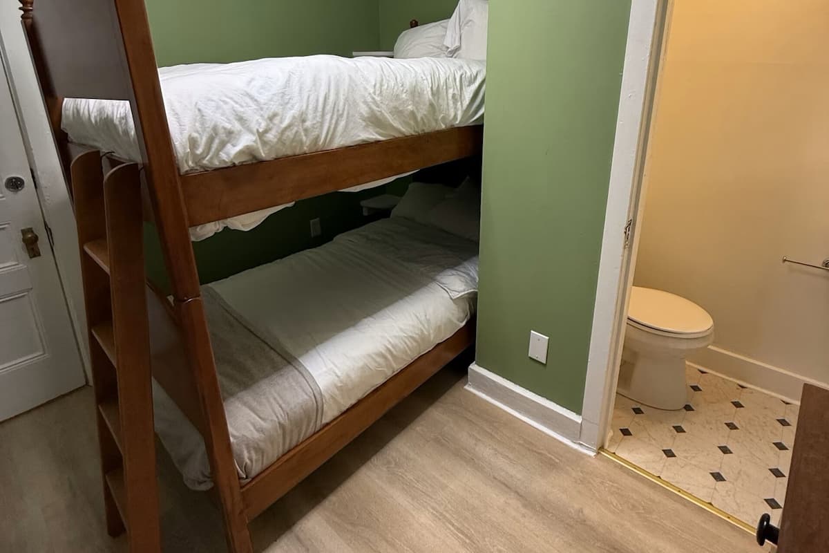 A bunk bed in a room with green walls, a wooden floor, and a white door leading to a bathroom.