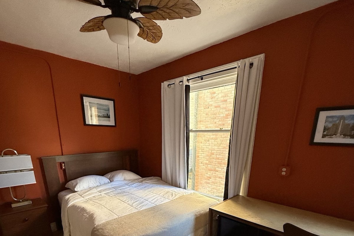 A bedroom with a bed, a desk, and a ceiling fan.
