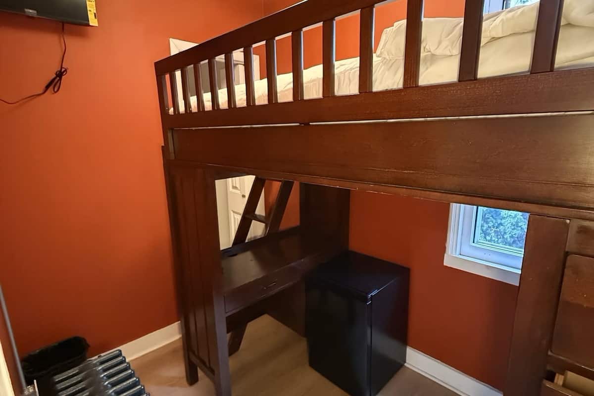 A room with a bunk bed, a desk, a radiator, and a window.