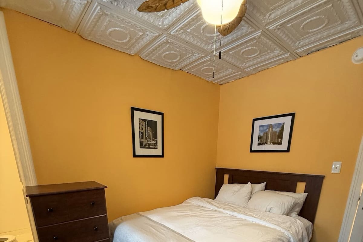 A bedroom with a bed, dresser, and ceiling with decorative elements.