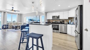 A modern kitchen with white cabinets, stainless steel appliances, and a bar area with stools. - ☀️Panoramic Gulf and Pool Views-Steps to Beach-Calypso 1-1709☀️ (Panama City Beach)