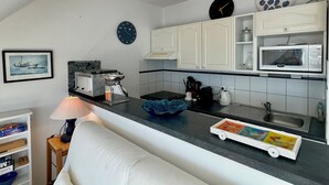 A compact kitchen with white cabinets, a microwave, a coffee maker, and a clock on the wall.