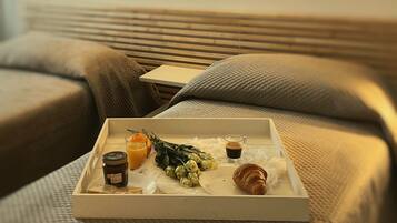 Un plateau de petit-déjeuner sur un lit, avec une bouteille de jus, un verre de jus d’orange, un croissant et un petit bouquet de fleurs.