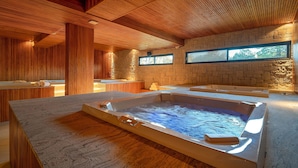 A spa area with a hot tub, wooden ceiling, stone walls, and a view of the outdoors. - Golden Tulip Canela OFICIAL (Canela)