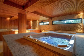 A spa area with a hot tub, wooden ceiling, stone walls, and a view of the outdoors.