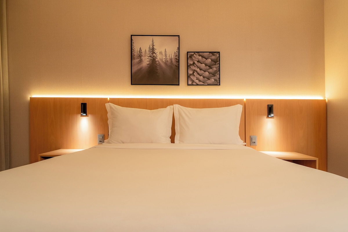A neatly made bed with two pillows, a wooden headboard, and two wall-mounted nightstands.