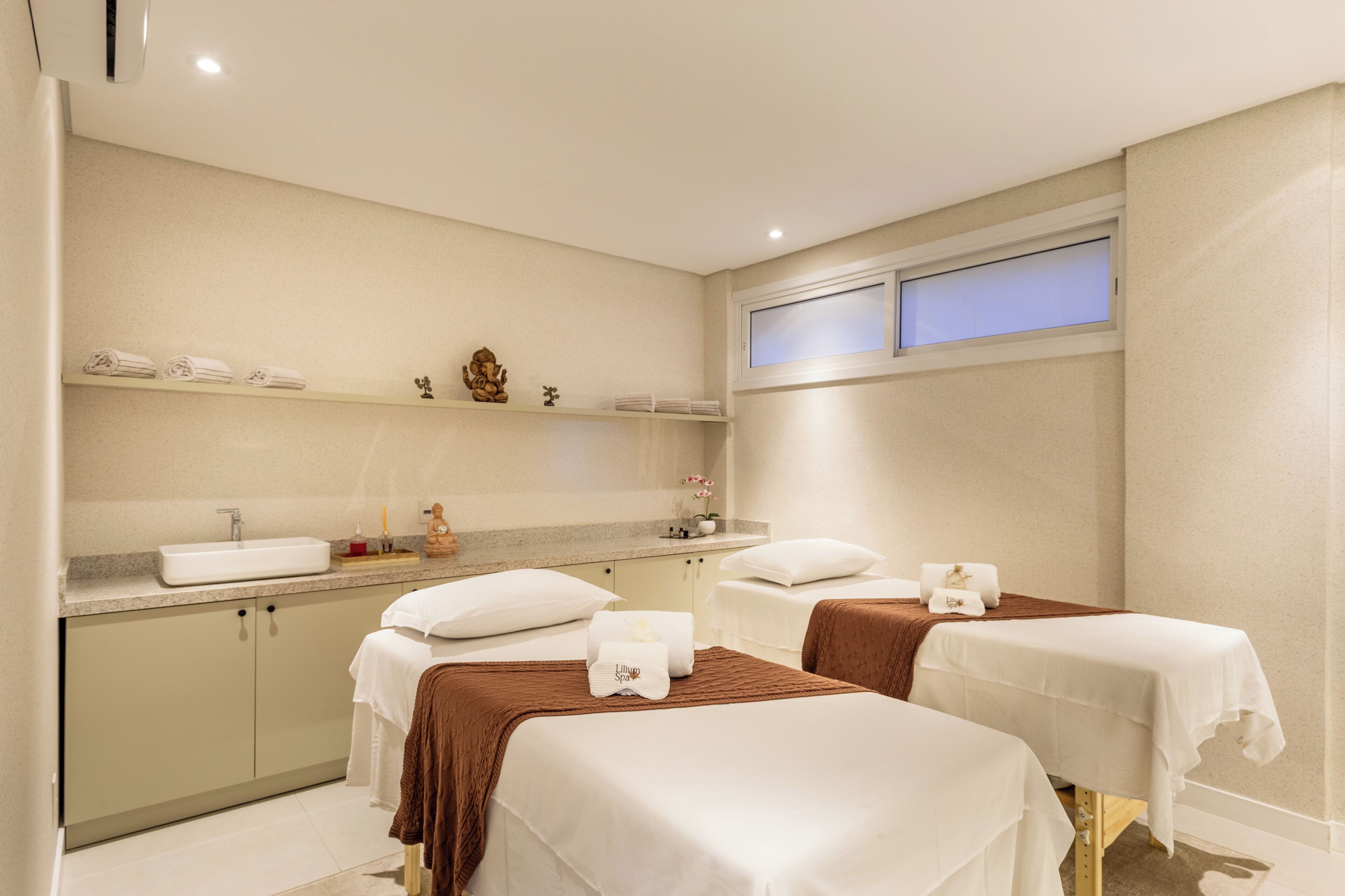 A hotel room with two beds, a sink, and a window.