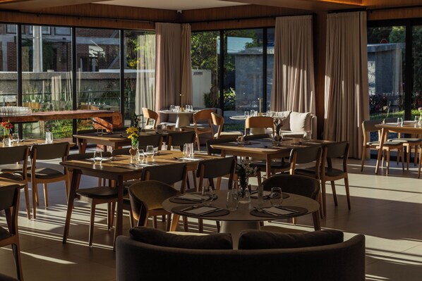 A restaurant with multiple tables and chairs, large windows, and a view of the outdoors.