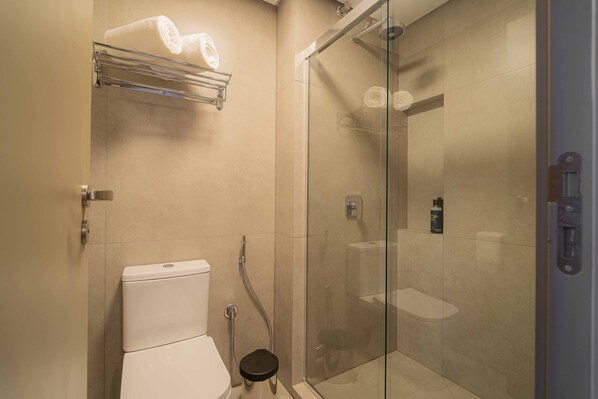 Un baño moderno con cabina de ducha de vidrio, inodoro y perchero.
