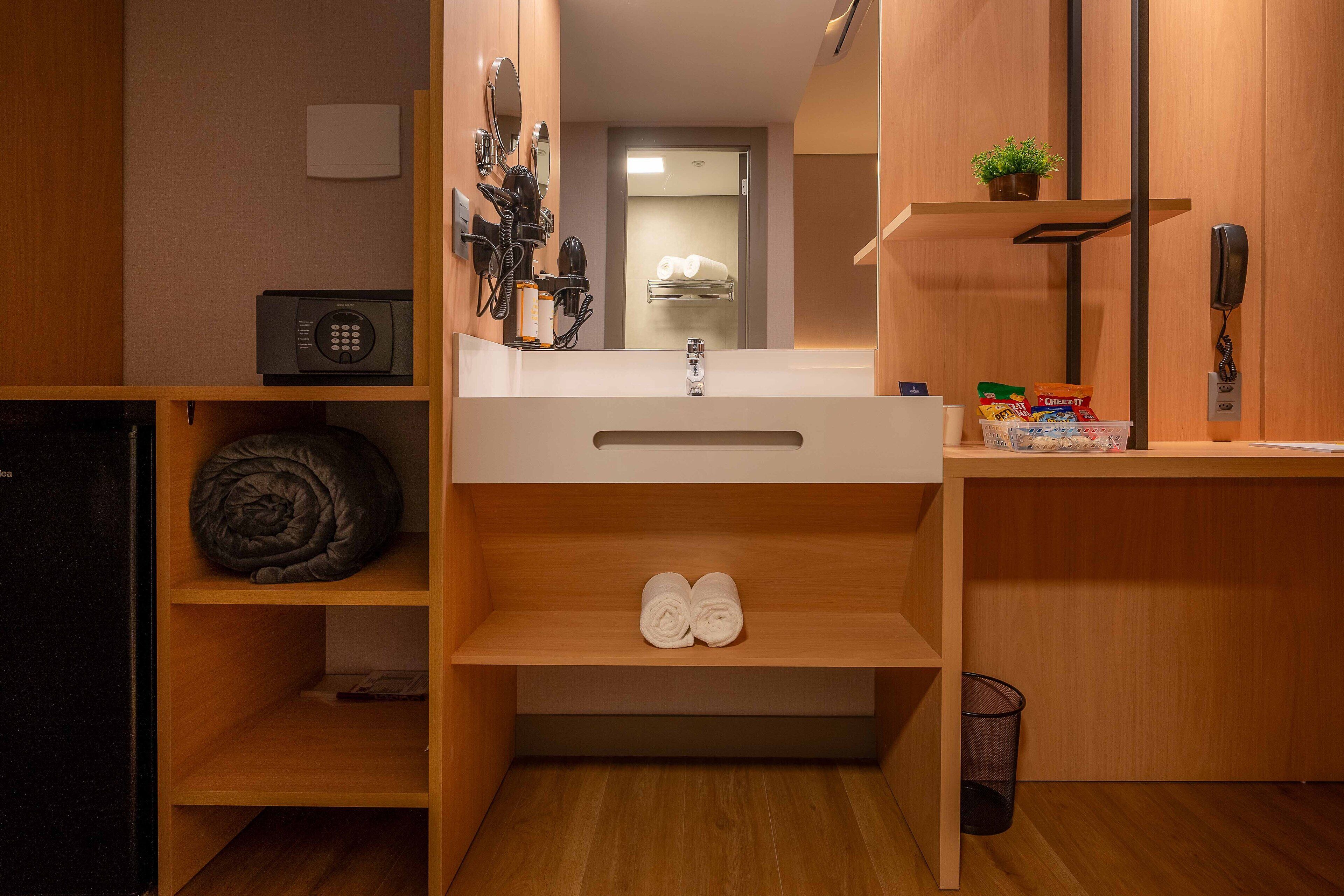 A compact hotel bathroom with a sink, towel rack, and a small trash bin.