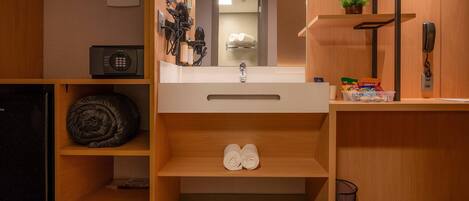 A compact hotel bathroom with a sink, towel rack, and a small trash bin.