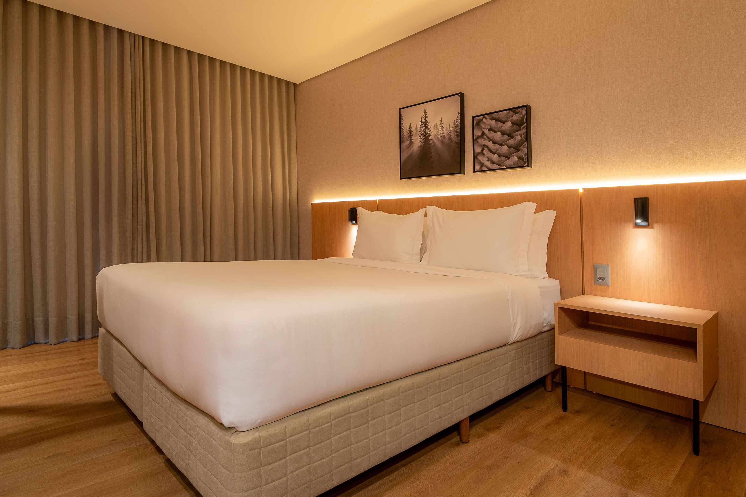 A neatly made bed with a headboard, a bedside table, and two framed pictures on the wall.