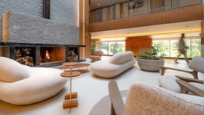 A spacious lobby with a fireplace, comfortable seating, and large windows offering natural light. - Golden Tulip Canela OFICIAL (Canela)