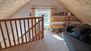 Ein gemütliches Dachzimmer mit Holzbalkendecke, einer Treppe, einem Bücherregal und einem Sofa.