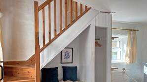 Eine Treppe mit Holzwangen führt zu einem Raum mit einem Bett, einem Heizkörper und einem Fenster mit Vorhängen.