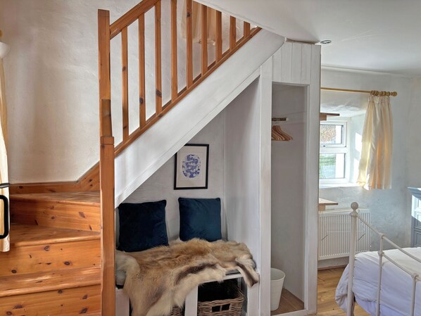 A staircase with wooden railings leading to a room with a bed, a radiator, and a window with curtains.
