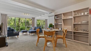 A modern living room with a dining area, large windows, and a bookshelf.