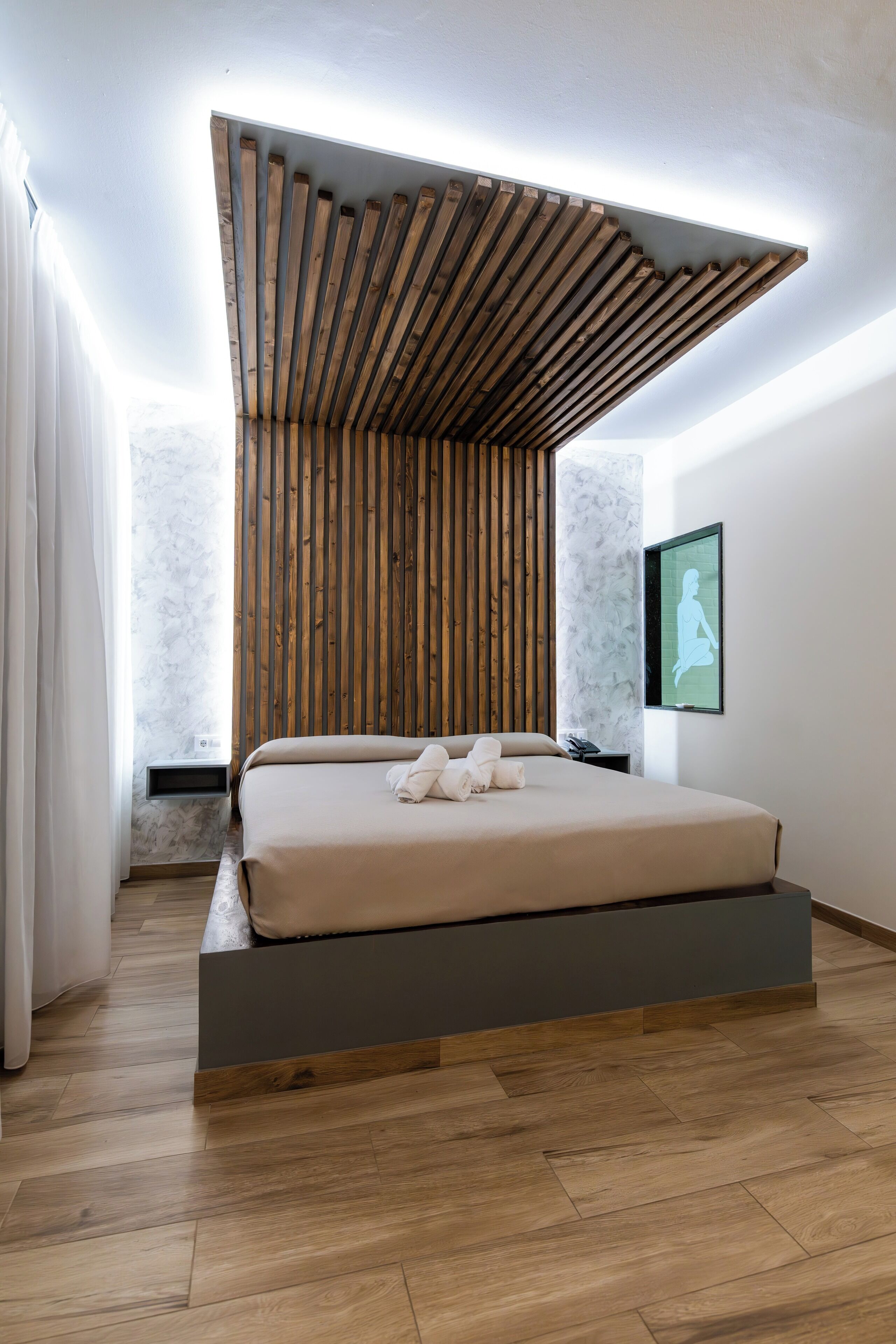 Un dormitorio moderno con techo de listones de madera, cama con plataforma gris, pared de mármol y una silueta enmarcada en la pared.