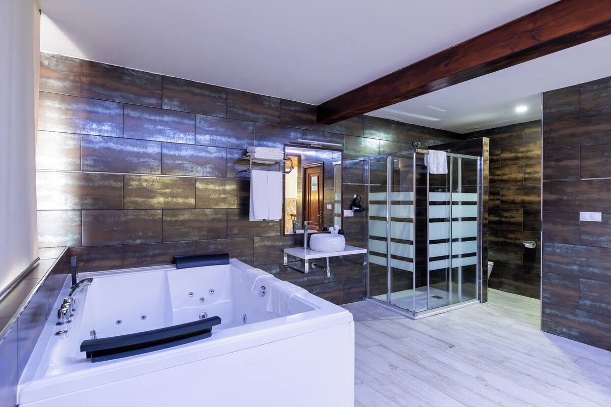 A modern bathroom with a large bathtub, a glass shower enclosure, and a wooden ceiling beam.
