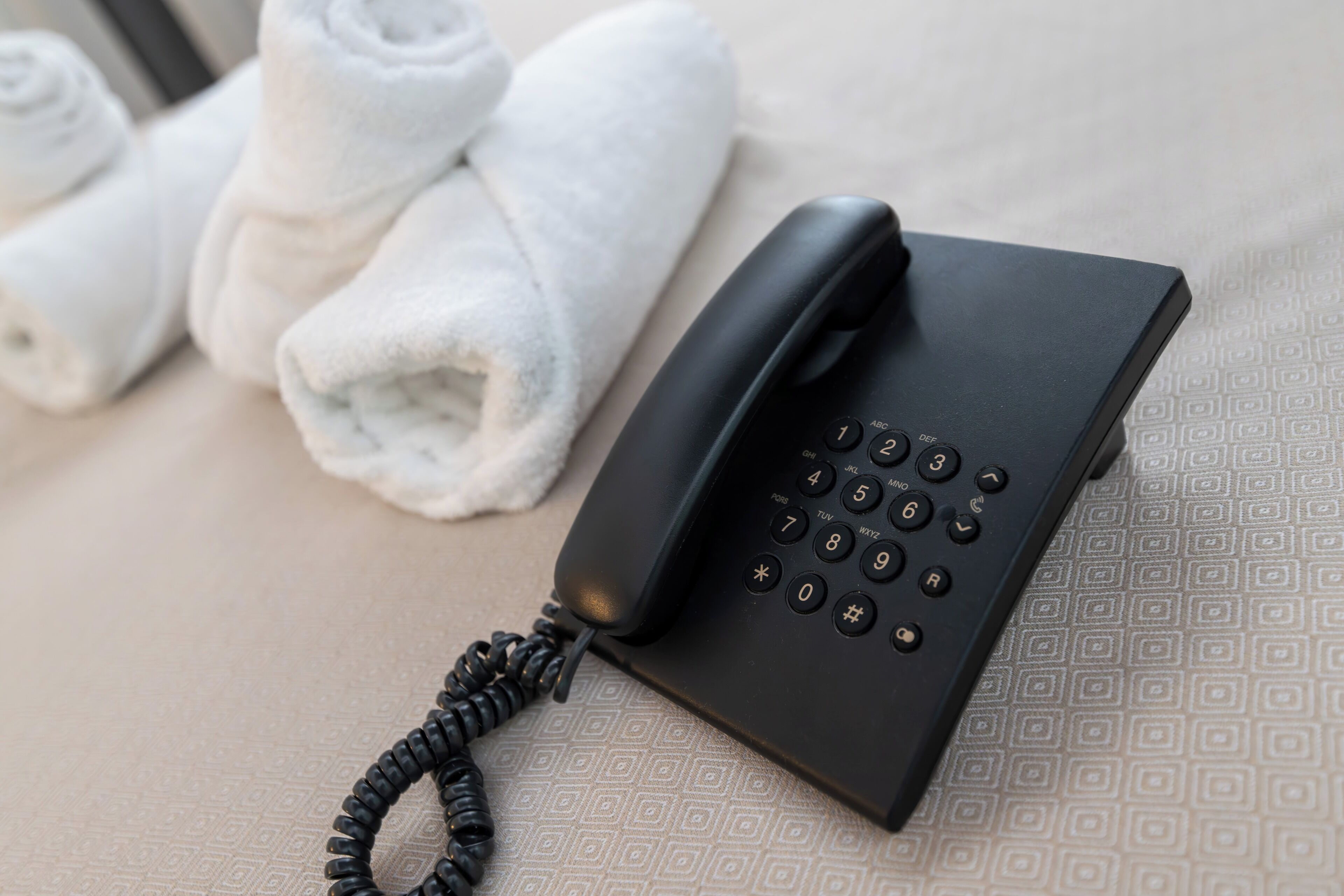 Ein schwarzes Telefon mit einem spiralförmigen Kabel auf einer gemusterten Oberfläche.