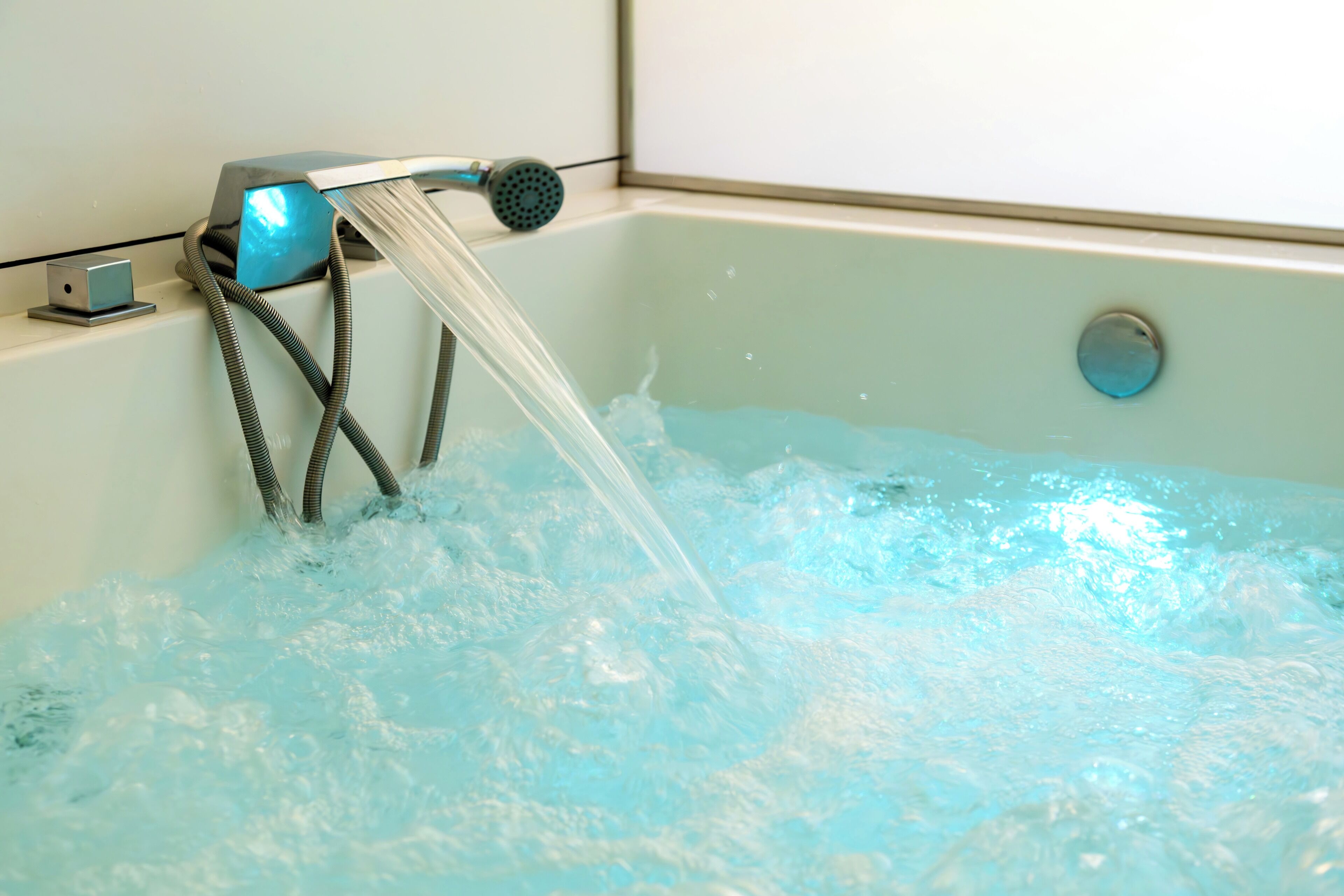 Una bañera con agua corriendo, un cabezal de ducha manual y un desagüe.