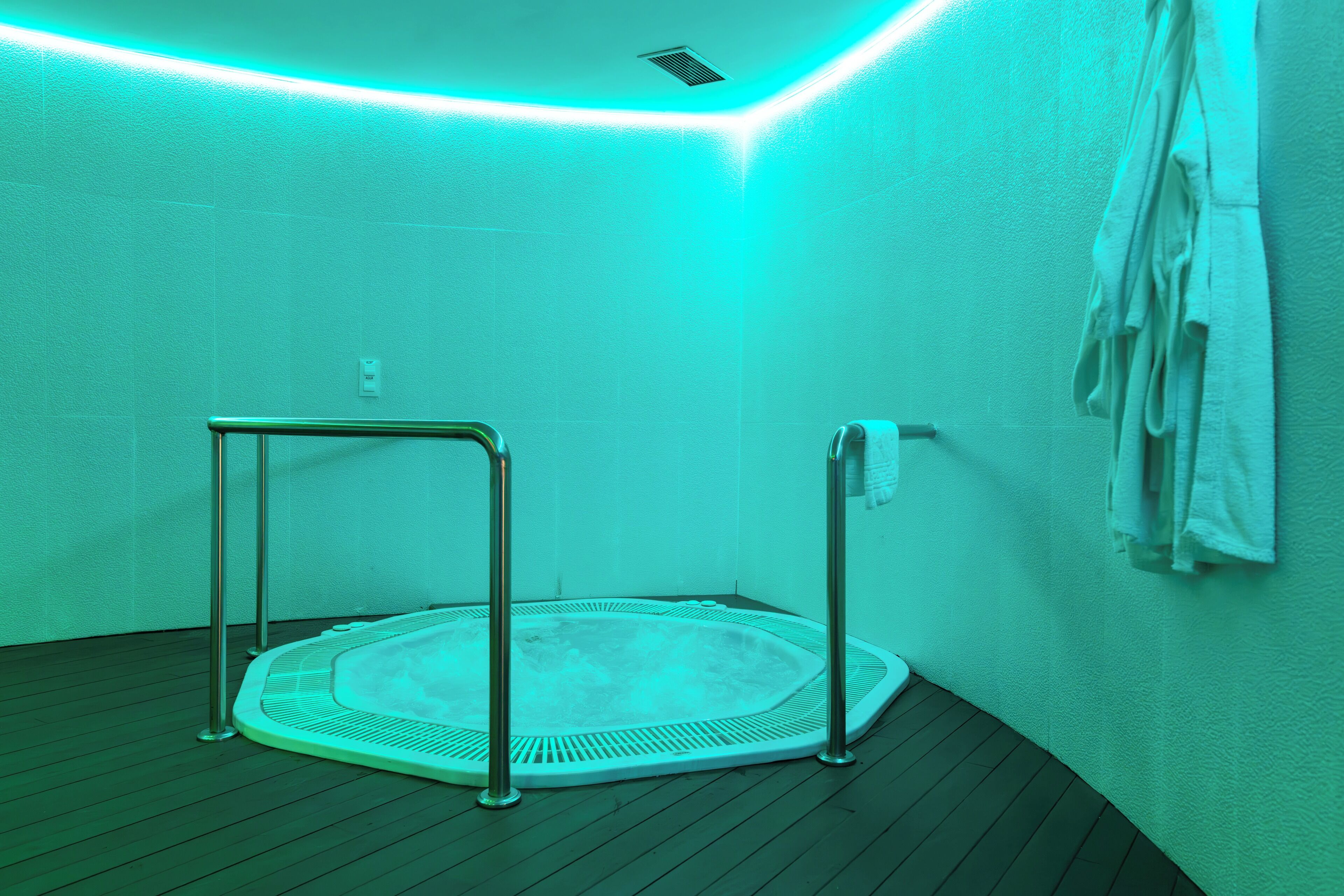 A spa room with a hot tub, metal railings, and towels on the wall.