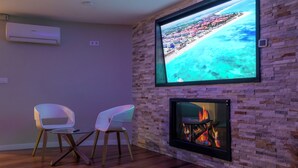 Een moderne woonkamer met een aan een bakstenen muur bevestigde televisie, een open haard en twee witte fauteuils.