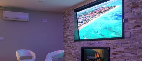 Una sala de estar moderna con un televisor instalado en una pared de ladrillo, una chimenea y dos sillas blancas.