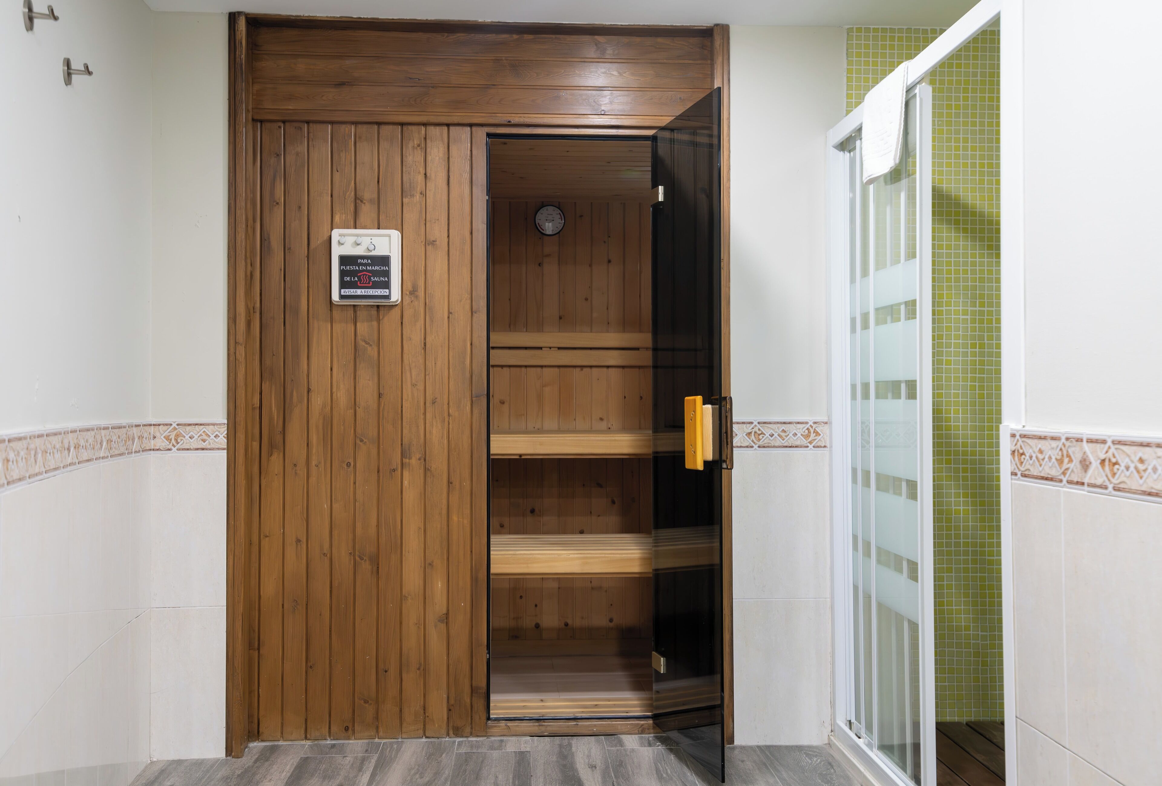 Puerta de sauna de madera con un letrero, puerta de cristal y pared con azulejos y detalles verdes.