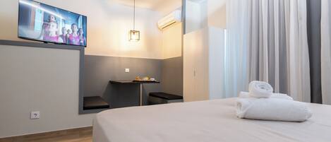 Une chambre d’hôtel moderne dotée d’un grand lit, d’un téléviseur à écran plat fixé au mur, d’un petit bureau avec une chaise et d’une fenêtre avec des rideaux.