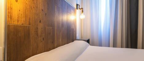 A hotel room with a wooden headboard, a bedside table with a remote control, and a wall-mounted light fixture.